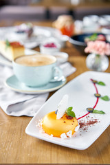 Yellow mousse-cake. Breakfast in the cafe, morning coffee. Cappuccino and lots of desserts on the table. French dessert, blueberry, mint and a piece of meringue on a white plate. Restaurant menu