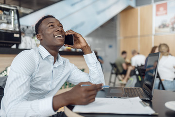 Ebony businessman talking by phone in office cafe