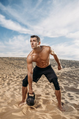 Athlete doing exercise with kettlebell in desert