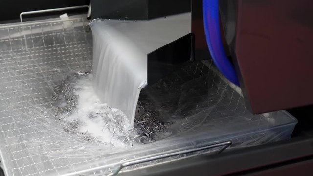 Rear side of CNC machine where liquid coolant is flowing out after use from machine with metal shavings, swarf filtered and then pumped back into the process.