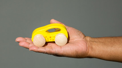 the outstretched hand of an African American man holding a yellow toy car isolated on a solid background