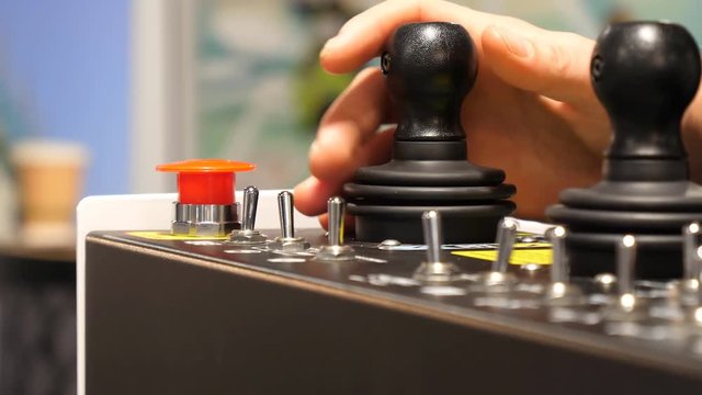 Close up of hand of man standing on moving training platform wearing VR headset (not seen) and holding cherry picker or boom lift control panel joystick.