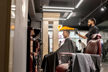 Fototapeta na wymiar Brutal guy in modern Barber Shop. Hairdresser makes hairstyle a man . Master hairdresser does hairstyle with hair clipper. Concept barbershop