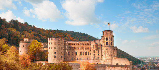 Side view of Heidelberg Castle, or Heidelberger Schloss in German language, in Autumn with golden leaves in the forest and nearby hills. Panoramic travel image