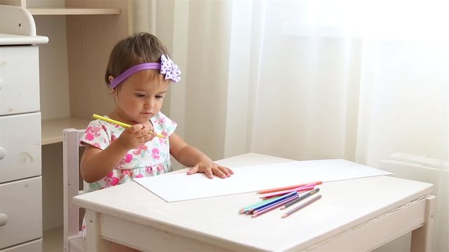 Little girl learning to draw in kindergarten with colored pencils sitting at a white table