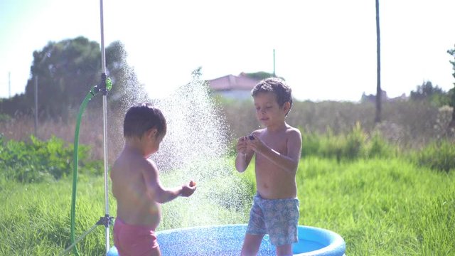 Two litle brothers playing in summer with a shower in the garden in a funny and joyful way