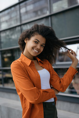 Fototapeta na wymiar Portrait of cheerful curly hair woman with beautiful smile and white teeth walking on street. Cute African American fashion model posing for pictures outdoors. Hair volume, natural beauty concept