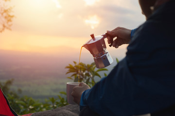 Male tourists pouring coffee from moka pot, men with coffee and beautiful natural background, tents, mountain peaks