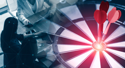 Business Target Goal For Success Strategy Concept - Red dart arrow hitting center goal on the dart board with business people working in background showing precision and success of business target.