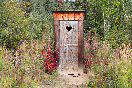 An outhouse in a wooded area with a heart window
