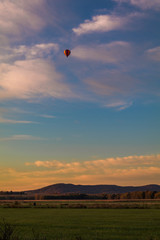 Rainbow hot-air balloon floats over field at sunrise, portrait