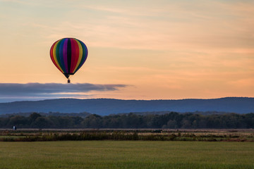 Rainbow hot-air balloon floats over field at sunrise