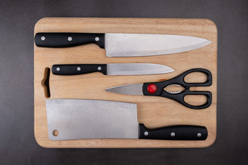 Set of kitchen knife and scissors on wooden chopping board, top view.
