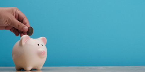 Hand insert coin in piggy bank on blue background, banner concept.