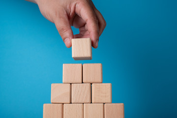 Hand arranging block on blue background. Business concept on progress or building something.