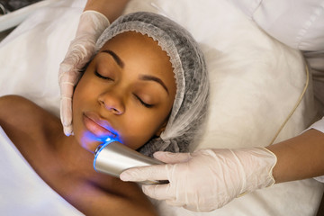 Ultrasound chromotherapy. Hardware cosmetology. Beautician carries out procedure for face skin...
