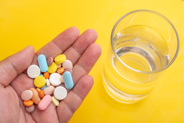 glass of water and multi color medical pills on yellow background