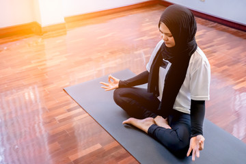 Young Muslim woman sitting in lotus pose and meditating with closed eyes during yoga classes on the...