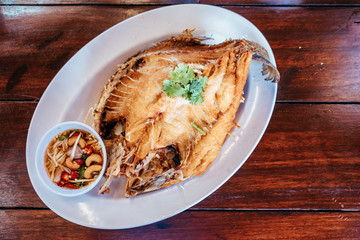 Deep fried Snapper topped with fish sauce in white dish serving on table. Pla kapong tod num pla....