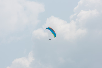 A blue paraglider flying in the background of the far sky white clouds