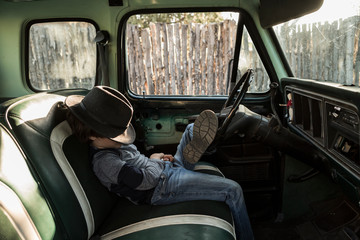 6 year old boy sitting in vintage pick up truck with hat covering his face