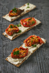 Three toasted breads with cream cheese and sun-dried tomatoes on a wooden table.