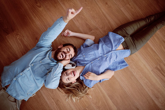 Top view of attractive caucasian couple lying on the floor, listening music over the headphones and singing.