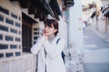 Young beautiful woman wearing white coat, standing and sleeping and posing with hands together while smiling with closed eyes at Korea.