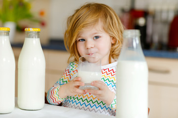 Adorable toddler girl drinking cow milk for breakfast. Cute baby daughter with lots of bottles....