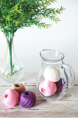 Eco-friendly cotton yarn. Glass jug with yarn. Items for female needlework on a white wooden table. Space for your text.