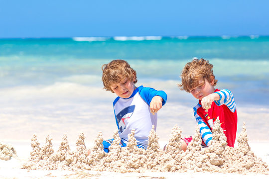 Two little kids boys having fun with building a sand castle on tropical beach on island. Healthy children playing together on their vacations. Twins, Happy brothers laughing and smiling