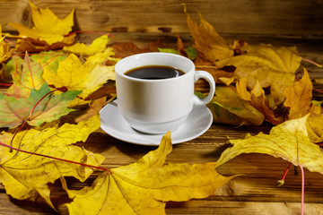 Cup of coffee and autumn maple leaves on wooden table. Autumn concept