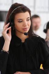 Three call centre service operators at work. Portrait of smiling pretty brunette woman at workplace...