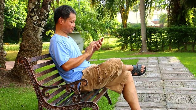 Thai man playing smart phone  in the garden, outdoor  Chiangmai Thailand