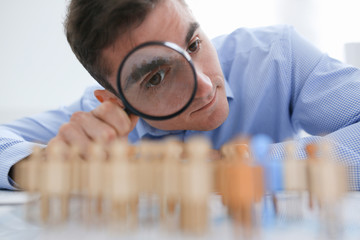 A businessman in blue shirt is holding a magnifying glass in his hand, is searching for personnel...