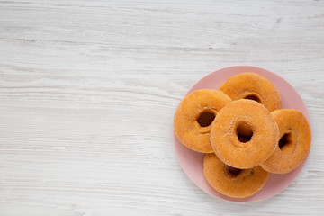 Homemade apple donuts ready to eat on a pink plate on a white wooden background, view from above. Top view, flat lay, overhead. Copy space.