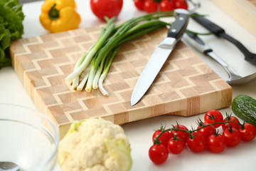 Knife and green onions for salad or fresh vegetable soup with vitamins are on wooden cutting board. Raw food and vegetarian food recipe book in modern society is a popular concept.