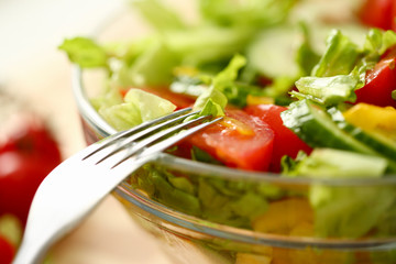Silver fork in plate mixes salad fresh vegetables seasoned with olive oil. Raw food and vegetarian in modern society is popular concept.