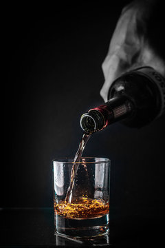  Pouring cognac or whiskey from the bottle into the glass against black background