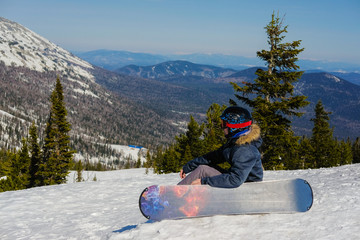 Fototapeta na wymiar Young snowboarder in the mountains on top. Active rest on a snowboard.