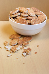 Fat cookies in a bowl, glass cup with milk, light brown wooden background.
