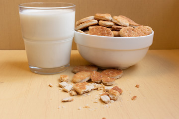 Fat cookies in a bowl, glass cup with milk, light brown wooden background.