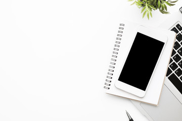 White office desk table with white smartphone with blank mockup screen, laptop computer, notebook...