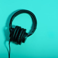 Black over ear headphones closeup on blue background, top view. Minimal music background, copy space