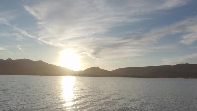 Dramatic sunset scenery over the lagoon with mountain silhouette in the background and a bird crossing over the sun in backlight, filmed in flat color profile