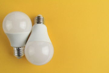 Two electric incandescent lamps in white matte color on a yellow background. Copy space.