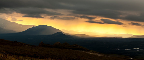 Sunset in the mountains, the rays of the sun breaking through the clouds. Kamchatka Peninsula, Russia