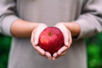 A woman holding a fresh red apple in hand