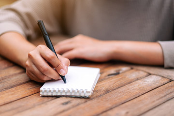 Closeup image of a woman writing on blank notebook on wooden table
