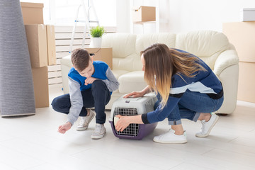 Slim young mother and little son launch their beautiful gray Scottish Fold cat into their new apartment in the living room. The concept of tradition with housewarming.